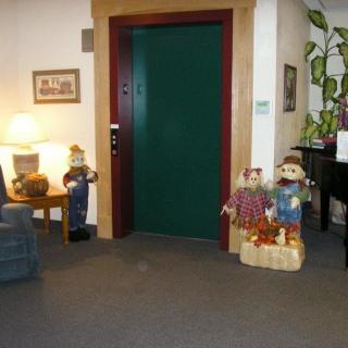 A cozy indoor space featuring an elevator, various decorations with an autumn theme, a lamp, and some seating.