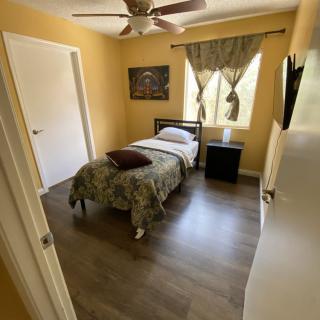 A cozy bedroom with a single bed, ceiling fan, and wooden flooring.