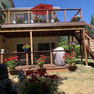 A two-level wooden deck with railings, potted plants, and stairs leading to a grassy backyard on a sunny day.