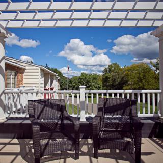 Two chairs under a pergola on a sunny patio with a view of the backyard.