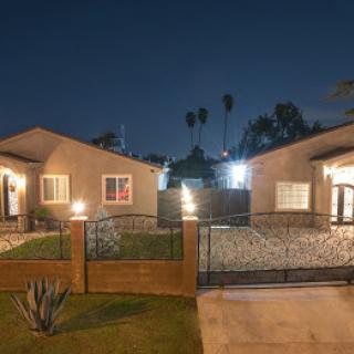 A picturesque view of two well-lit houses at night, surrounded by a landscaped yard and palm trees.