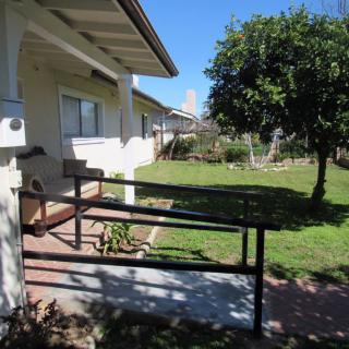 A sunny view of a house with a ramp leading to the entrance, surrounded by a grassy yard and trees.