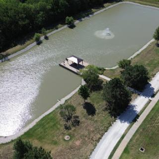 A serene aerial view of a pond with a dock and fountain, surrounded by lush greenery.