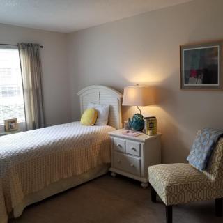 A cozy bedroom with a bed, lamp, and chair near a window.