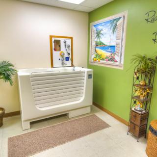 A bathroom interior featuring a bathtub, artwork, and decorative plants against a green wall.