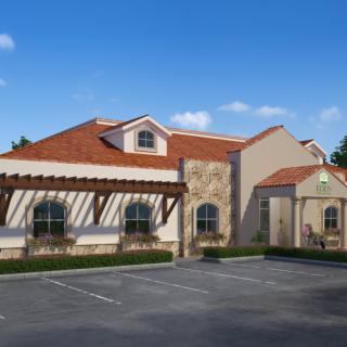 A Mediterranean-style restaurant building with a terracotta roof, stone accents, and an adjacent parking lot under a clear blue sky.