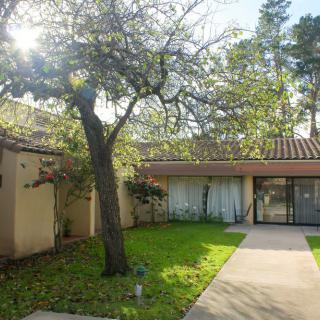 A sunny view of a house surrounded by trees with a small garden in the yard.