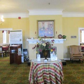 A cozy lobby area featuring a round table with a floral centerpiece, a painting above a fireplace, and comfortable seating.