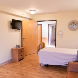 A clean and organized hospital room with wooden flooring, featuring a bed, television, and essential furniture.