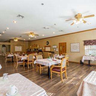 A spacious dining room with neatly arranged tables and chairs, featuring wood flooring and ceiling fans.