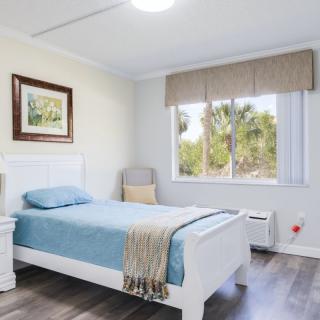 A bright and minimalist bedroom featuring a single bed with blue bedding, a window allowing natural light, and simple decor.