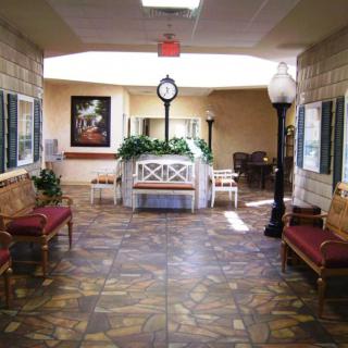 A well-lit hallway featuring benches, decorative plants, and a central clock.