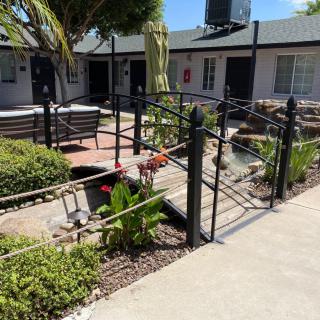 A serene courtyard with a pathway leading to benches, surrounded by plants and enclosed by a fence.