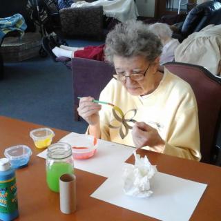 An elderly person engaged in a painting activity at a table indoors.
