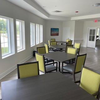 A bright and airy dining area with multiple tables and chairs, illuminated by natural light from large windows.