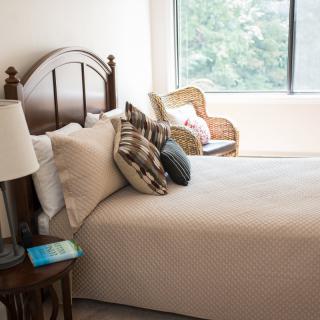 A cozy bedroom with a neatly made bed, decorative pillows, and a large window.