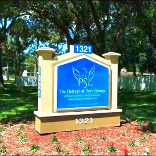 A school sign with the text 'PSL The School at MPI College' displayed in an outdoor setting surrounded by trees and well-maintained landscaping.