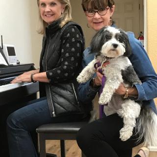 Two women enjoying a moment together at the piano with a dog.
