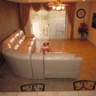 A cozy living room with a large sectional sofa and a coffee table, featuring elegant curtains and a ceiling fan.