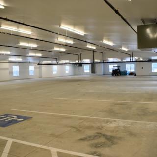 An empty indoor parking garage with bright lighting and a few parked vehicles.