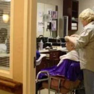 A hairdresser styling an elderly person's hair in a wheelchair at a salon.