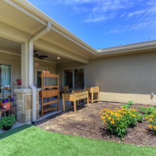 A sunny backyard patio with raised planters and a garden area featuring vibrant flowers.