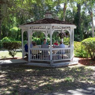 A group of people sitting inside a gazebo surrounded by trees and greenery in a park.