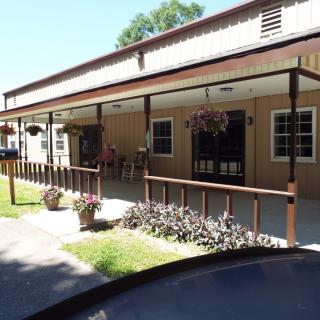 A sunny day view of a building with a covered porch and hanging plants.