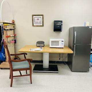 A cozy break area featuring a chair, table, microwave, and refrigerator.