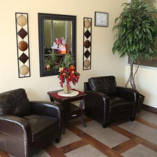 A cozy waiting room with two leather chairs, a small table with flowers, a mirror, and decorative wall art.
