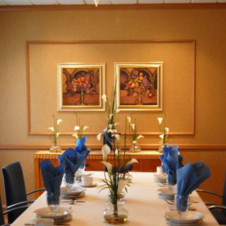 An elegantly set dining table with blue napkins, candles, and framed artwork on the wall.