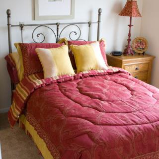 A cozy bedroom with a neatly made bed featuring red and yellow bedding and pillows, accompanied by a nightstand and lamp.
