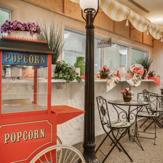 A charming indoor cafe setting with a vintage popcorn cart and decorative flowers.