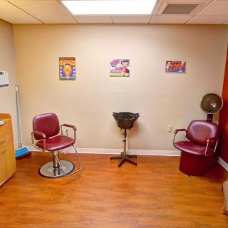 An interior view of a hair salon featuring chairs, a hair dryer, and a wooden floor.
