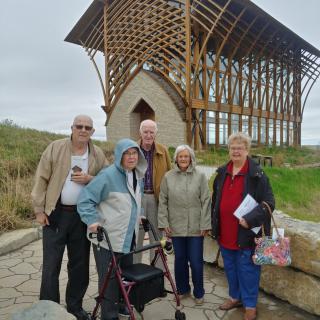 A group of elderly people posing in front of an outdoor architectural structure.