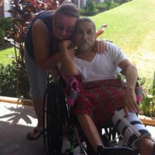 A person in a wheelchair with a leg brace is accompanied by another person outdoors.
