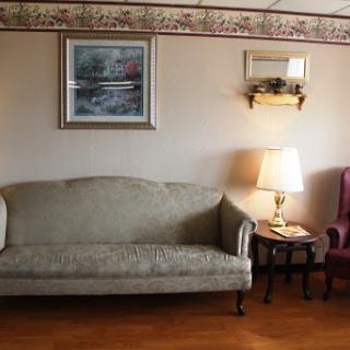 A cozy living room setup featuring a beige sofa, a purple armchair, a table lamp, and decorative artwork on the wall.