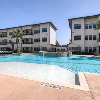 A modern apartment complex featuring a refreshing outdoor swimming pool under a clear blue sky.