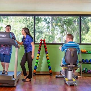 People engaging in physical therapy with a trainer in a well-equipped indoor facility.