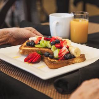 A breakfast plate featuring toast topped with fresh fruit and berries, accompanied by orange juice and coffee.