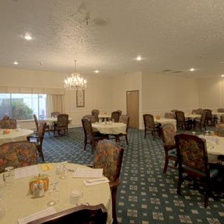 An empty dining room with neatly arranged tables and chairs, featuring a chandelier and carpeted floor.