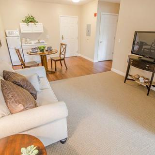 A cozy living room with a sofa, television, and a small dining area, featuring warm lighting and neutral decor.