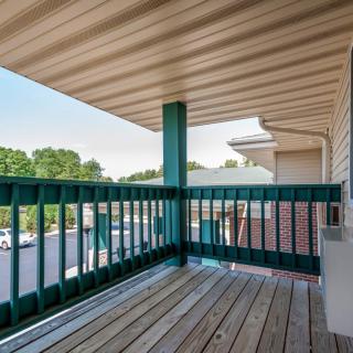 A covered balcony with a wooden floor and railing, offering a view of the surrounding area.