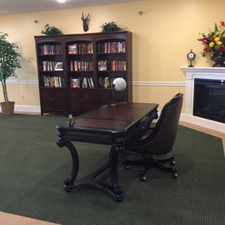 A cozy office space featuring a wooden desk, comfortable chair, and a bookshelf filled with books. A fireplace adds to the ambiance of the room.