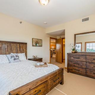 A cozy and bright bedroom with wooden furniture, featuring a bed, dresser, and soft lighting.