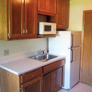 A compact kitchen area with wooden cabinets, a microwave, and a refrigerator.