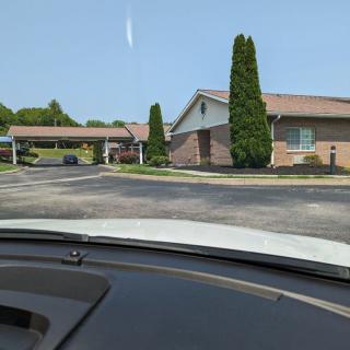 A view from inside a car showing a building with a parking area and tall trees.