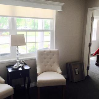 A cozy living room corner with two white chairs, a lamp, and a side table by the window.