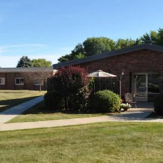 A brick residential building with a well-maintained lawn and pathway surrounded by shrubs and trees on a clear day.