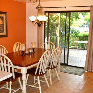 A cozy dining room with a wooden table and white chairs, featuring a chandelier and sliding glass doors leading to a deck.